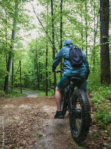 A man on an electric fatbike rides through a wet forest. Back view.