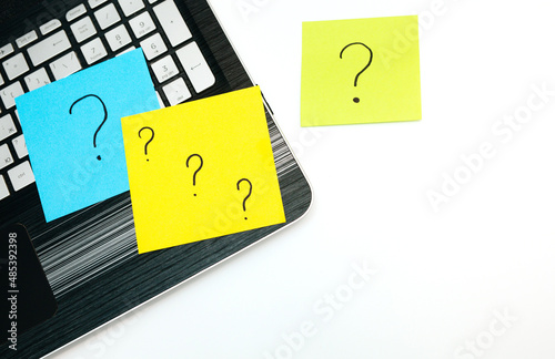 Laptop and memo pieces of paper with drawn question marks on white background. Top view