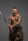 Violent tattooed warrior with sword isolated on gray background