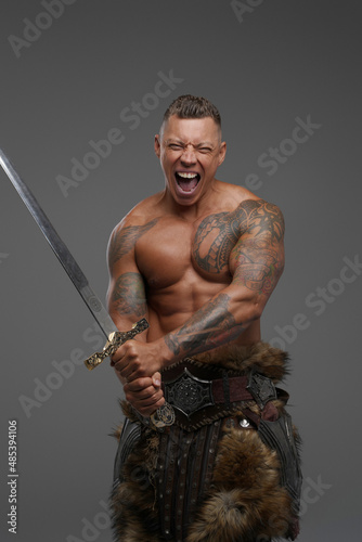 Violent tattooed warrior with sword isolated on gray background