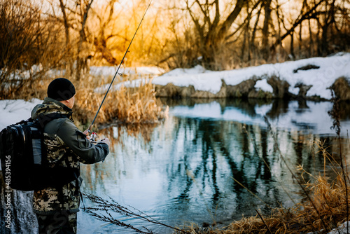 A fisherman fishing with a spinning rod on the riverbank in winter