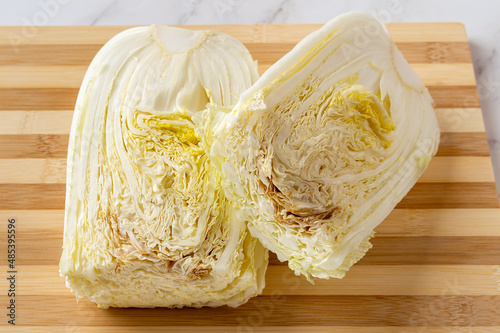 Rotten napa cabbage cut in half on a chopping board. The cabbagehead spoils from the inside. The rotting inside a chinese cabbage close-up. Food waste, spoiled vegetables concepts. photo