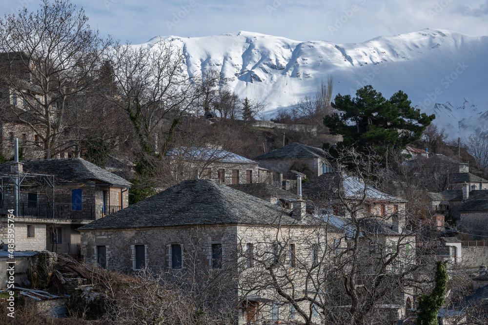 Traditional houses of the old village of Kalarites in Tzoumerka Greece by a mountain covered in snow