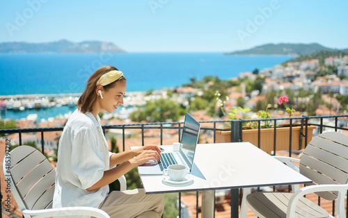 Foto Young woman using laptop computer at cafe balcony of resort hotel with sea view,