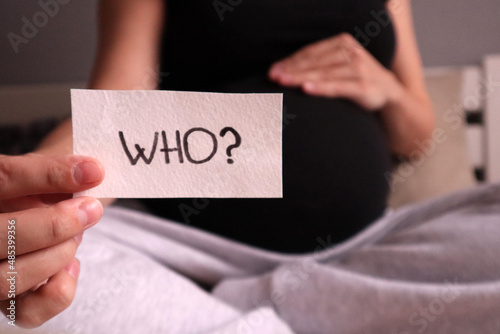 A pregnant woman holds a card with the question "Who?". Photo for gender party