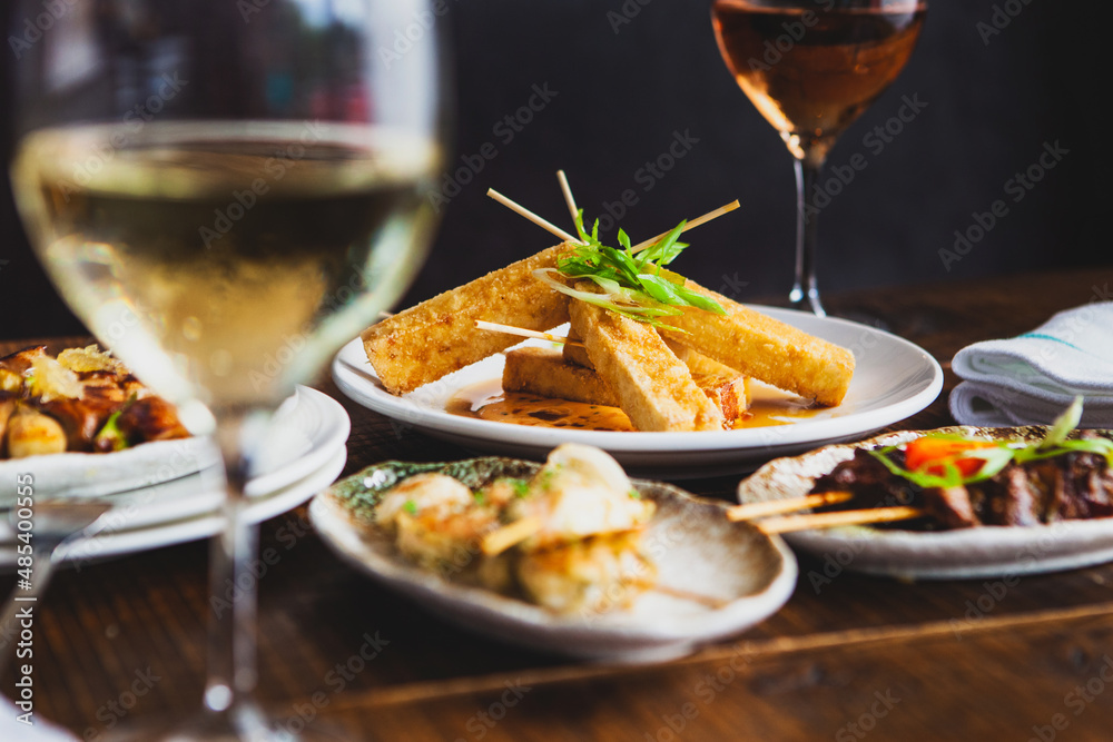 Fried tofu appetizer sitting on a restaurants wooden table with glasses of wine