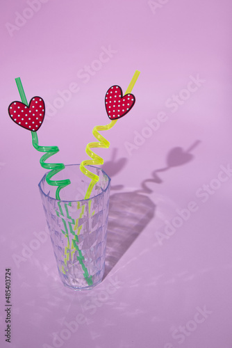 A glass with love straws for two on a pink background. All this creates a shadow.