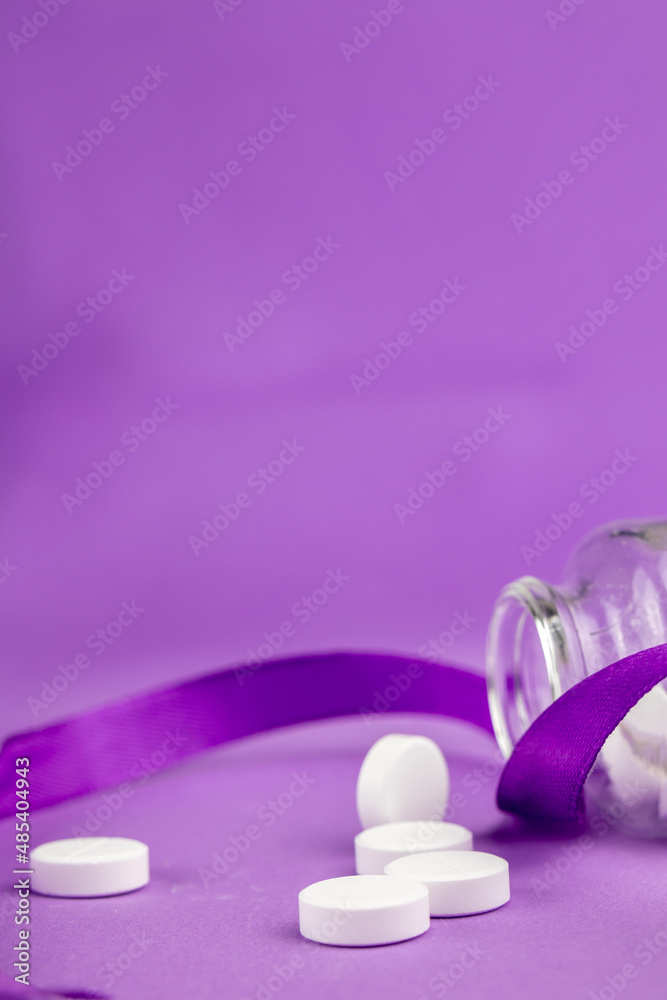 White pills in a jar with purple ribbon on a purple background. White pills in a jar with purple ribbon on a purple background.
