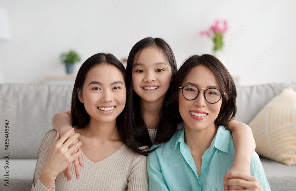 Portrait of joyful Asian family of mature mother, adult daughter and little granddaughter smiling at camera at home Portrait of joyful Asian family of mature mother, adult daughter and little granddaughter smiling at camera at home