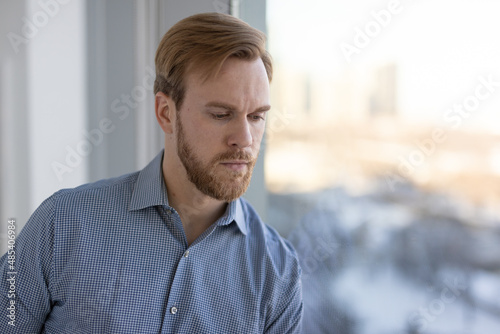 Caucasian man feeling sad and depressed standing by a window