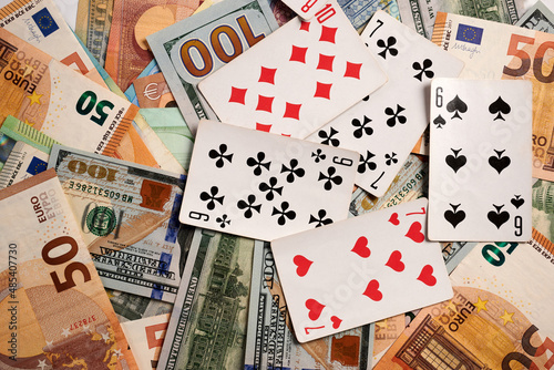 Playing cards on dollar and Euro bills. Dollar and Euro banknotes under gambling cards. Euro and dollar paper bills lay on background under casino and hazard symbols. Cost of gambling business.