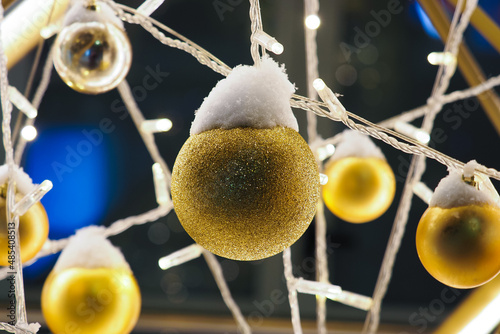 Gold balls and garlands hanging under snow. Christmas installation