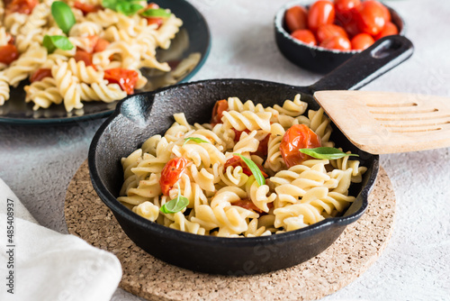 Pasta with tomatoes and basil in a pan and in a plate and a bowl with tomatoes on the table. Mediterranean cuisine.