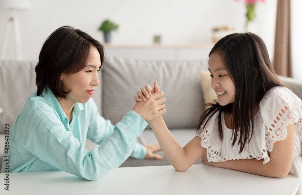 Stressed little Asian girl arm wrestling with her grandmother, having conflict, fighting at home Stressed little Asian girl arm wrestling with her grandmother, having conflict, fighting at home