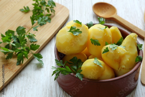 Cocked potatoes in brown clay bowl at the table, decorated with fresh green parsley