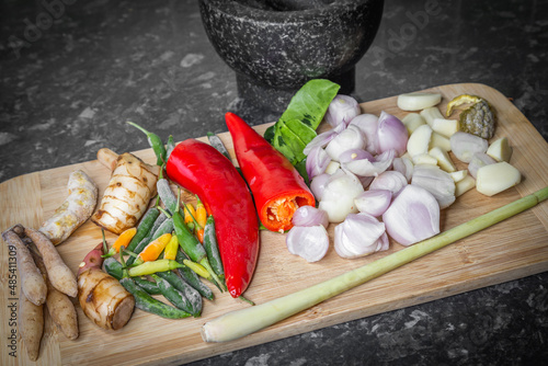 Thai green curry paste ingrediant including chillies, galangal, chinese key, lemongrass, shallots, garlic, tumeric, kaffir lime leafs, red peppers, red curry on a wooden board with  mortar and pestle photo