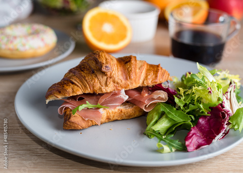 Still life with croissant with prosciutto and green salad and coffee. Healthy breakfast concept.