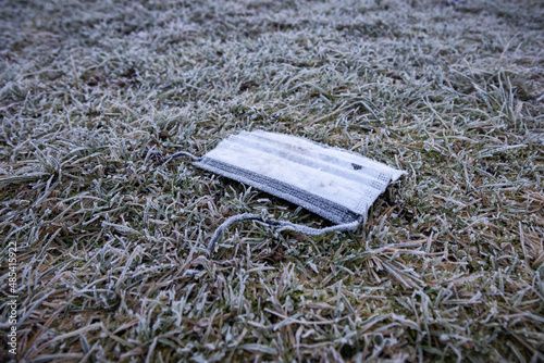 Face mask garbage on the ground. frosty grass in winter season photo