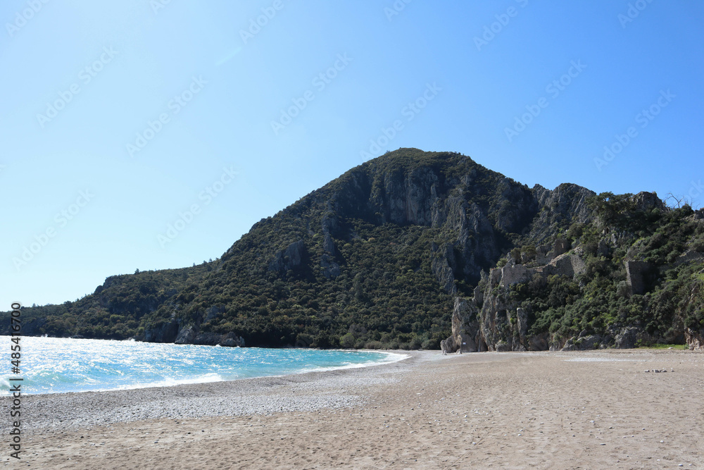 Fototapeta premium pebble beach of Cirali, Turkey and mediterranean sea with mountain and clouds in spring sunny day