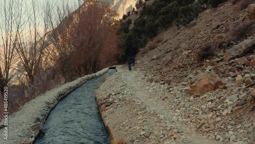 A man walking alongside of a small river stream in the mountains