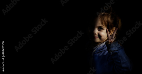 The little girl making a victory sign. Black background and the little girl.