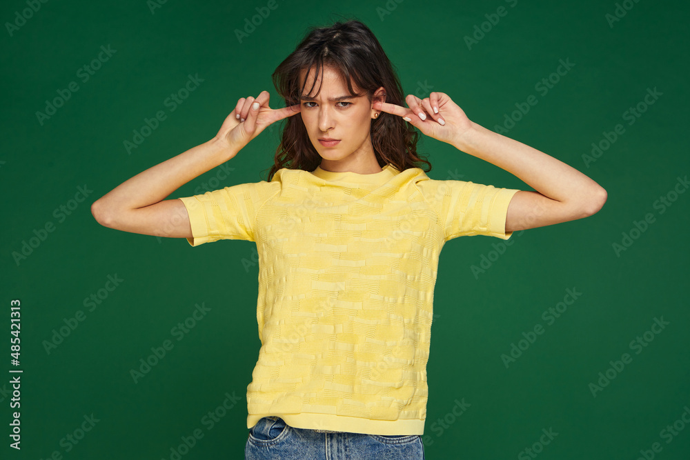 Annoyed offended young girl close plug ears avoid unpleasant information, refuse to listen on green studio background