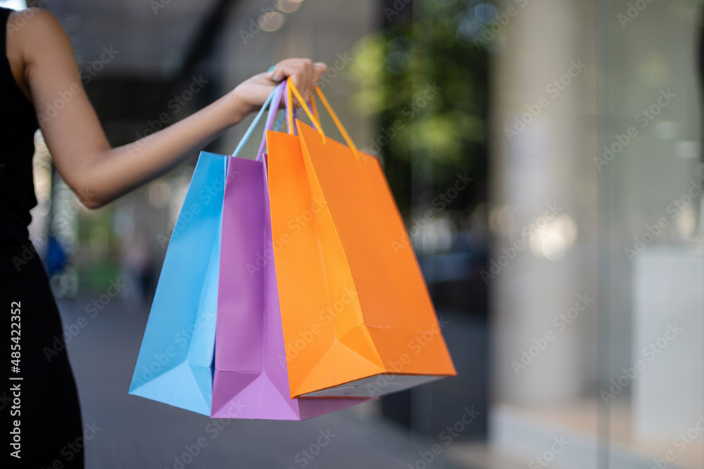 Close-up of multicolored blue, purple, and orange shopping bags in an African-American woman's hand outdoors in front of a mall