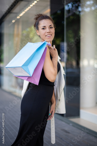 portrait of a smiling African-American woman with a blue and purple bag slung over her shoulder, looking at the camera outdoors