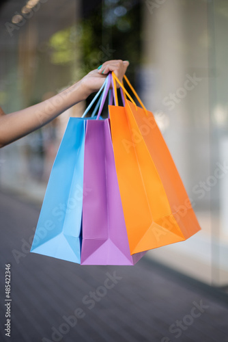 Close-up of colorful shopping bags in an African-American woman's hand outdoors near a mall, shot vertically