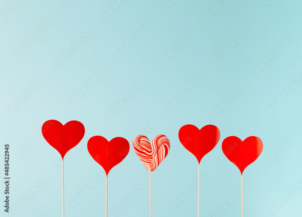 Red paper hearts on the wooden sticks with a heart-shaped lollipop in between on a blue background. 