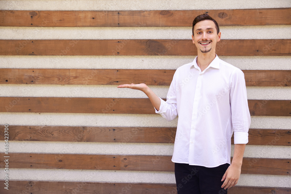 lifestyle, emotions, advertisement, gesture and people concept - A happy Caucasian bearded man in a white shirt and black pants holding something in palm on a brown ribbed background with copy space lifestyle, emotions, advertisement, gesture and people concept - A happy Caucasian bearded man in a white shirt and black pants holding something in palm on a brown ribbed background with copy space