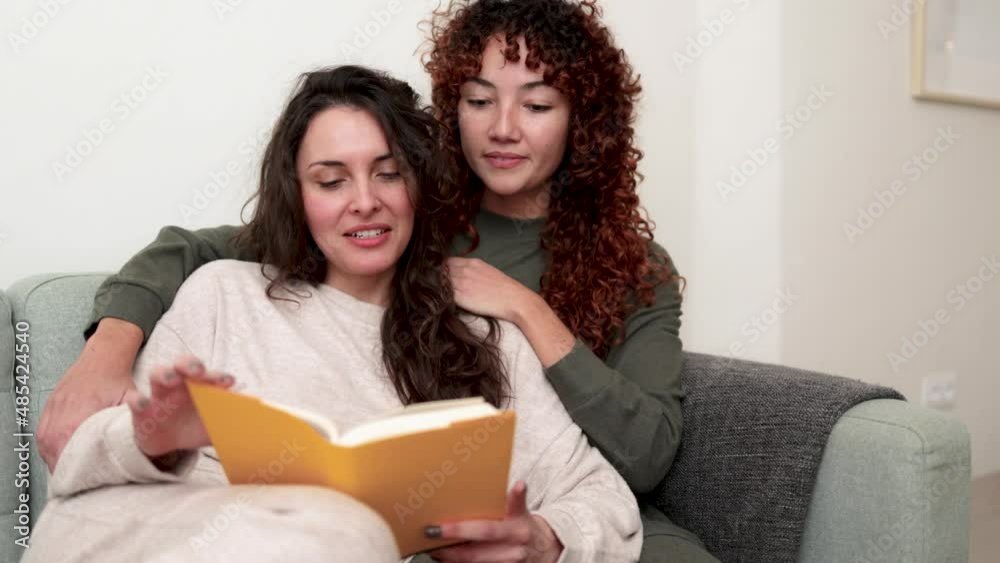 LGBT hispanic lesbian couple reading a book indoor at home - Gay love relationships concept LGBT hispanic lesbian couple reading a book indoor at home - Gay love relationships concept