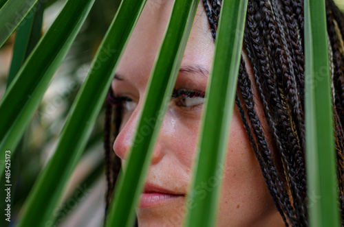 girl with afro braids behind a palm leaf