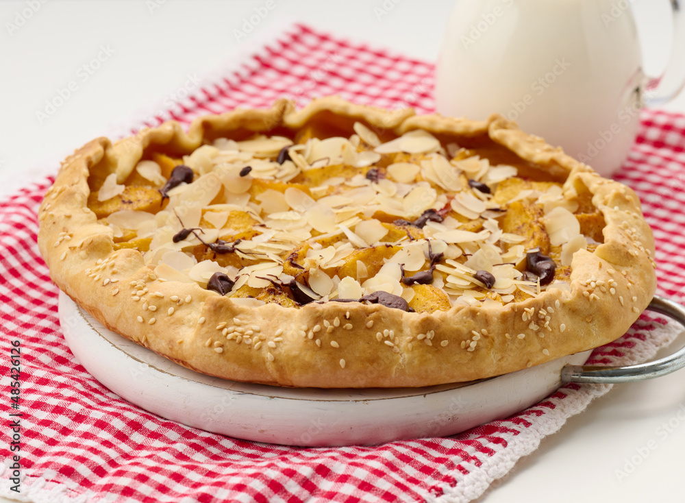 baked round pie with apple pieces, sprinkled with almond flakes on a white table baked round pie with apple pieces, sprinkled with almond flakes on a white table