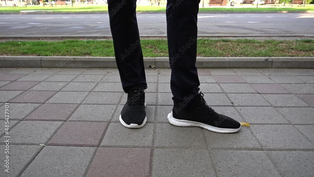 a young man is standing on the street in black pants and black sneakers with a white platform on a summer sunny day. legs close-up. a young man is standing on the street in black pants and black sneakers with a white platform on a summer sunny day. legs close-up.