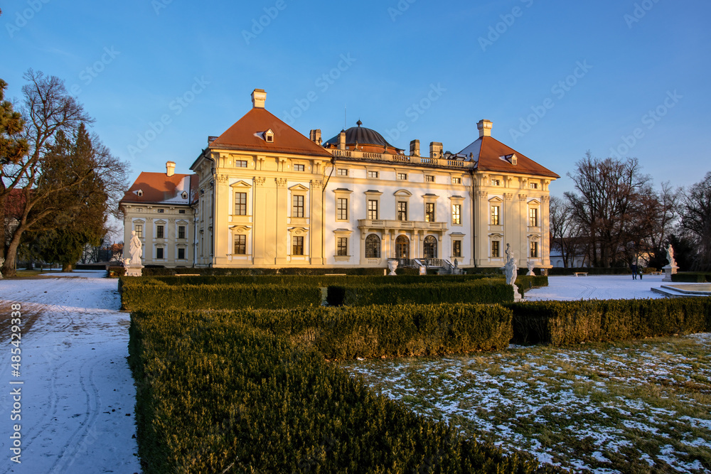 Slavkov Castle in the Czech Republic illuminated by the sun in winter. Snow lies in the park and garden in front of the castle.