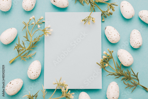 Stylish empty card, whitel Easter eggs, flowers blossoms on blue paper background flat lay. Easter greeting card mock up. Postcard template photo