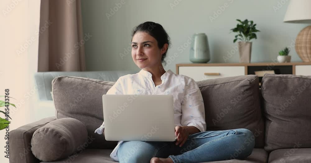 Young Indian freelancer sit on sofa with laptop working at home. Beautiful woman put wireless computer on laps smile typing text, do telework, chatting on-line, share messages in social media concept Young Indian freelancer sit on sofa with laptop working at home. Beautiful woman put wireless computer on laps smile typing text, do telework, chatting on-line, share messages in social media concept