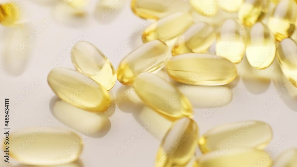 Omega-3 gold pills falling on white plate. Vitamin E. Pharmaceutical industry. Pills and drugs. Pharmaceutical industry. 4K, UHD Omega-3 gold pills falling on white plate. Vitamin E. Pharmaceutical industry. Pills and drugs. Pharmaceutical industry. 4K, UHD