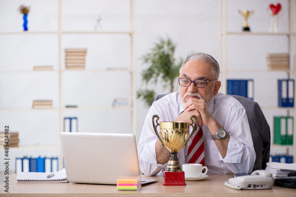 Old male employee being awarded with golden cup Old male employee being awarded with golden cup