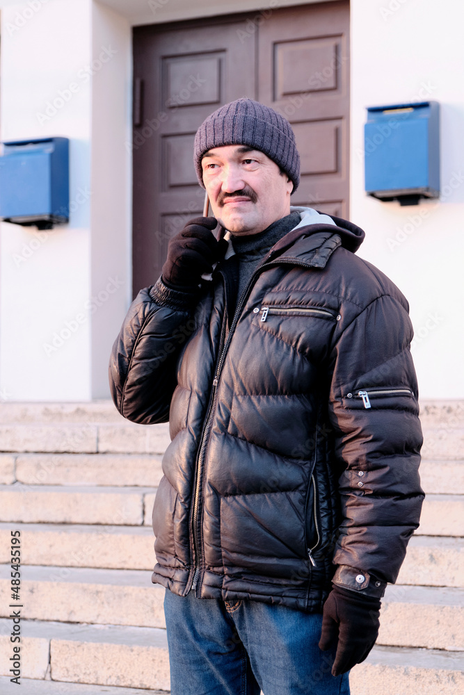 Senior asian man wearing knitted hat and warm jacket talking mobile phone outside.