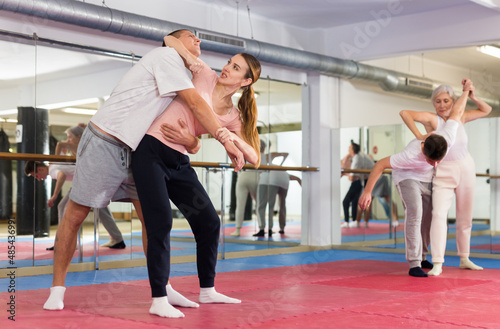 Concentrated young woman paired with male partner in self defense training, practicing basic elbow kick to chin during back grab