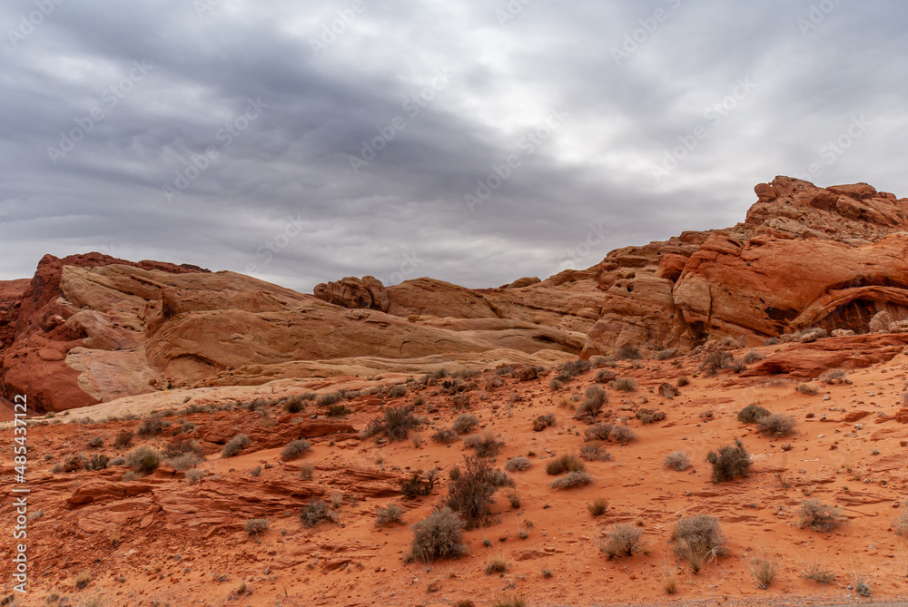 Overton, Nevada, USA - February 25, 2010: Valley of Fire. Heavy rainy gray cloudscape gathers over red rock mountainous outcrop rising out of dry red desert floor with greenish shrubs.