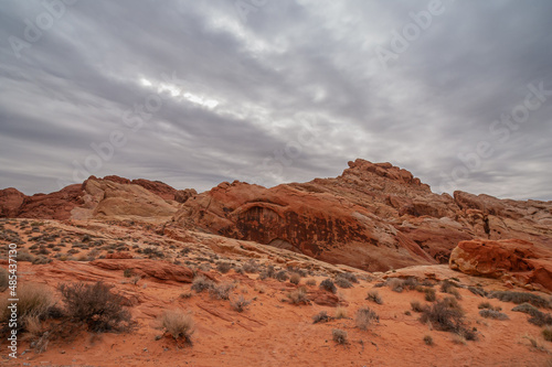 Overton, Nevada, USA - February 25, 2010: Valley of Fire. Heavy rainy gray cloudscape gathers over red rock mountainous area cropping out of dry red desert floor with greenish shrubs.