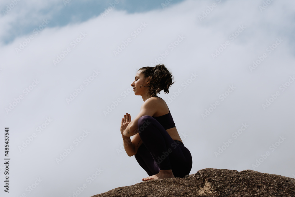 Woman doing yoga exercise asana pose on a top of a mountain cloud sky. Woman doing yoga exercise asana pose on a top of a mountain cloud sky.