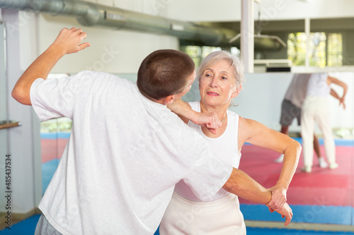 Senior woman exercising elbow strike on man during self-protection training.