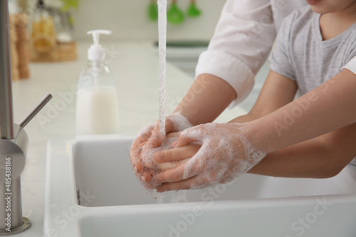 Mother and daughter washing hands with liquid soap together in kitchen, closeup