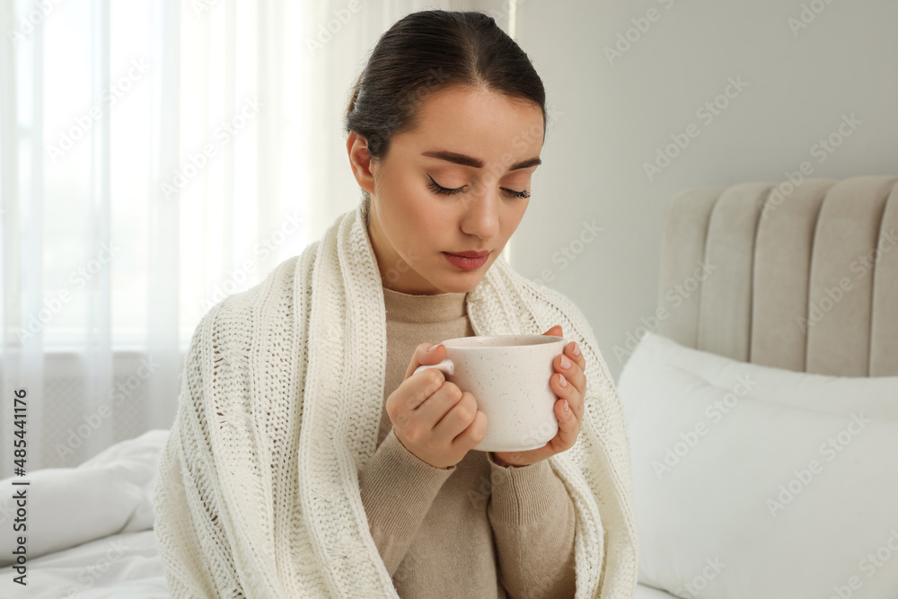 Beautiful young woman with cup of drink wrapped in knitted plaid at home Beautiful young woman with cup of drink wrapped in knitted plaid at home