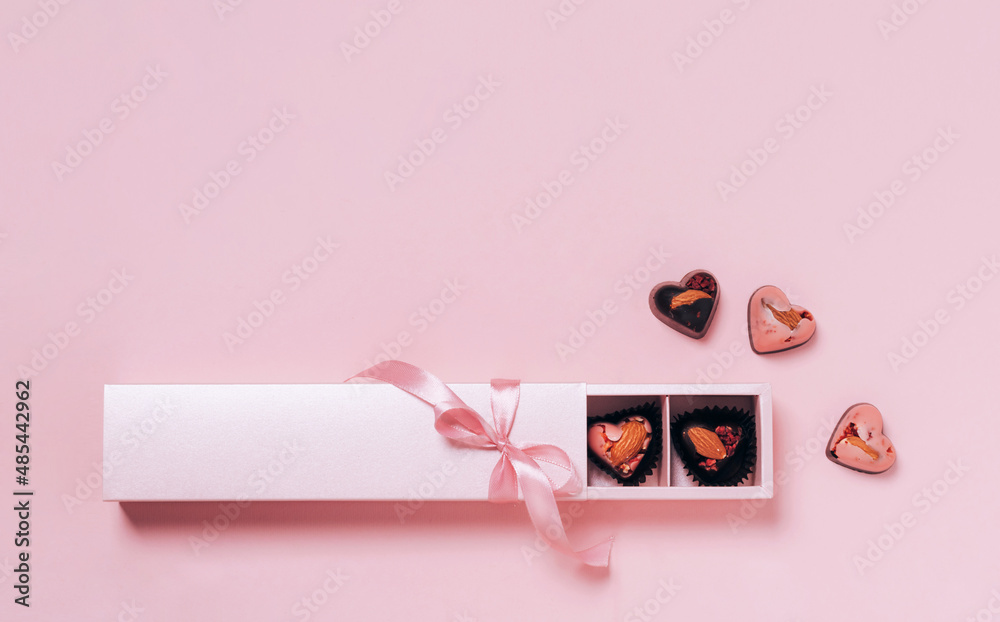 Chocolate candy hearts festive box satin ribbon bow on pink background. Flat layout copy space. Holiday concept Chocolate candy hearts festive box satin ribbon bow on pink background. Flat layout copy space. Holiday concept