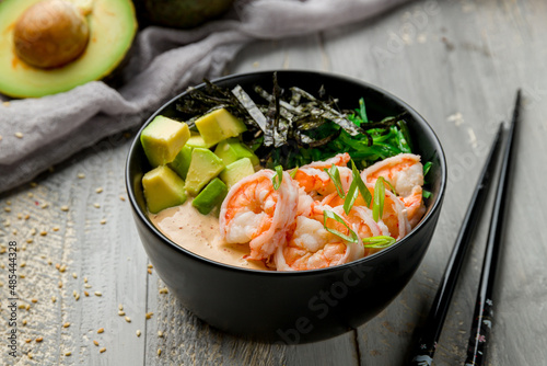 Poke with shrimps, avocado, chukka and sauce with rice on black bowl on grey wooden table